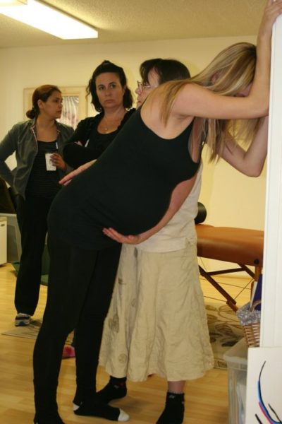 The hand in front is lightly on the lower abdomen. The hand in back is lightly on the sacrum. 